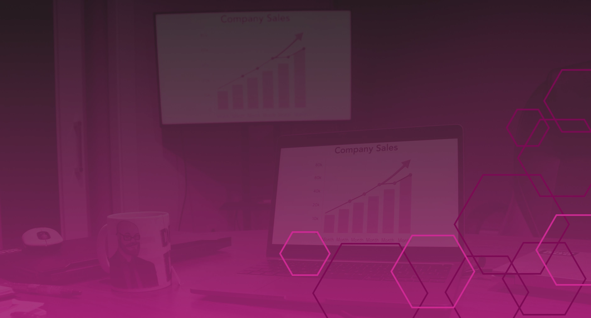 Laptop and monitor displaying upward-trending company sales charts, magenta overlay
